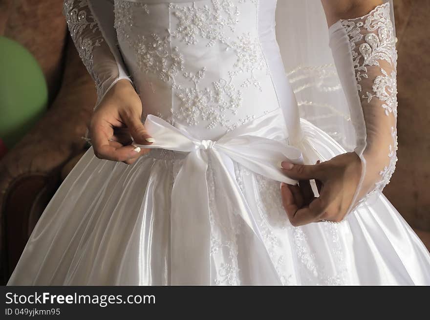 Hands of the bride fasten a bow on wedding dress