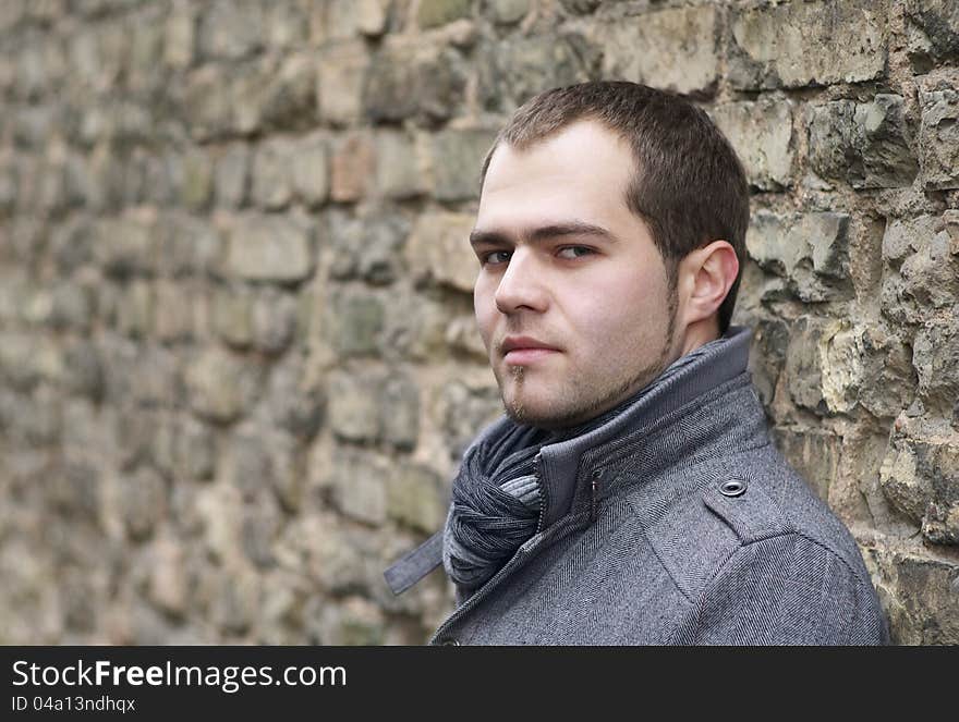 Young Man In Gray Coat Posing Near Old Wall