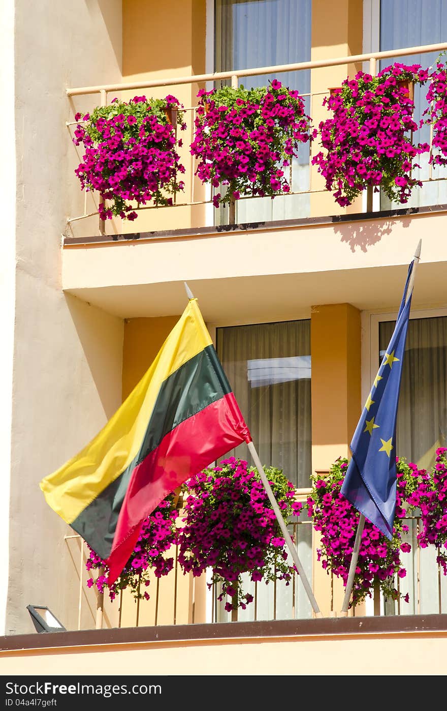 Lithuania and European Union flag hanging under building balcony with flowers.