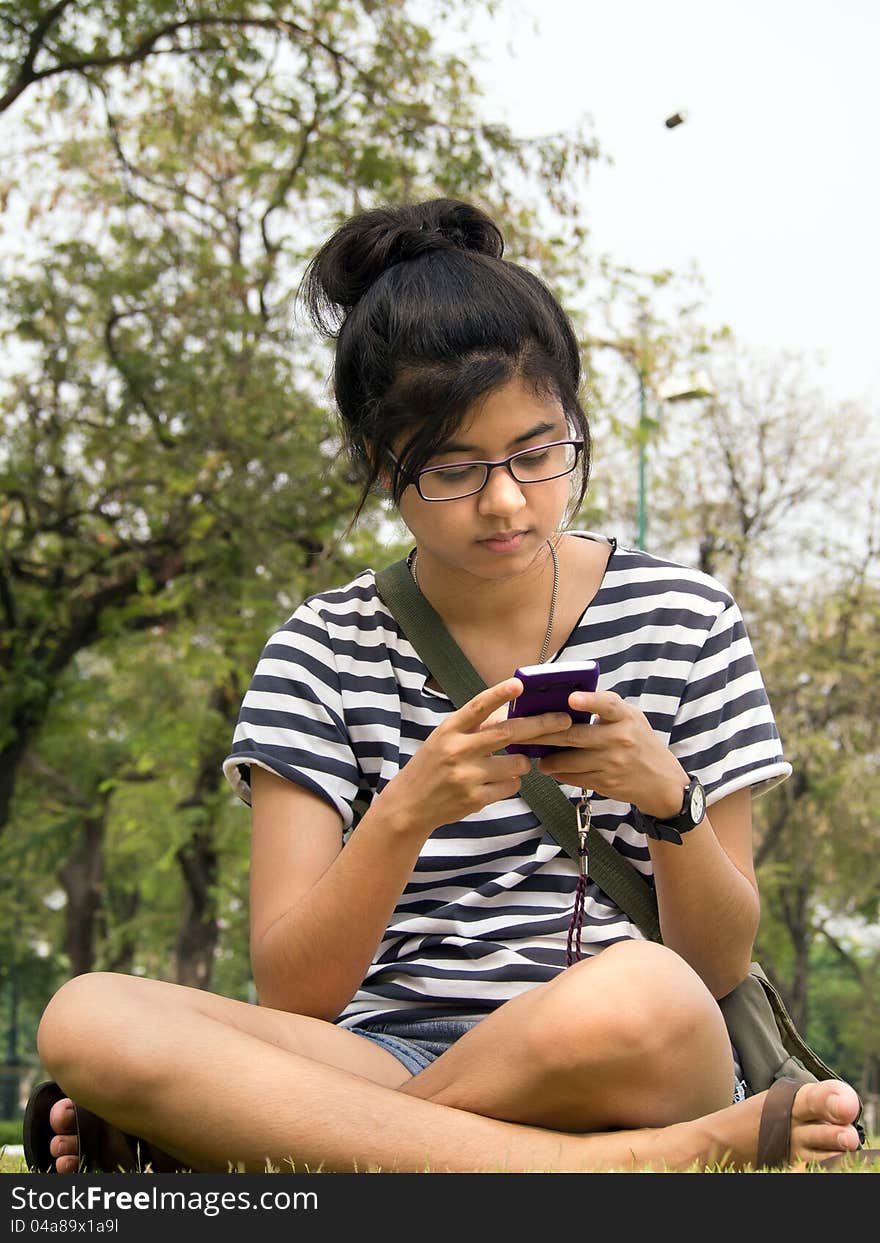 Woman sit on grass sending / receiving a text message / email on her mobile / cellular phone. Woman sit on grass sending / receiving a text message / email on her mobile / cellular phone.