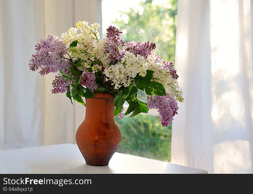 Bunch of lilac in ceramic jug against summer window. Bunch of lilac in ceramic jug against summer window