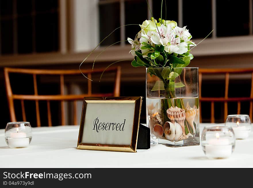 A wedding bouquet in a vase filled with water and sea shells on a reserved table. A wedding bouquet in a vase filled with water and sea shells on a reserved table