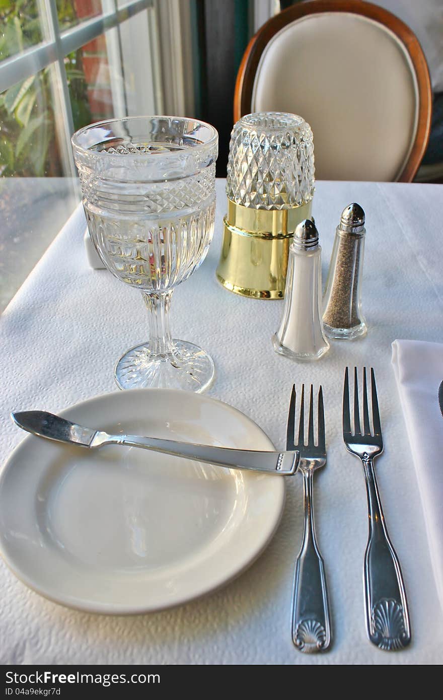 Silverwear, a folded napkin and a crystal glass filled with water on a restaurant table. Silverwear, a folded napkin and a crystal glass filled with water on a restaurant table