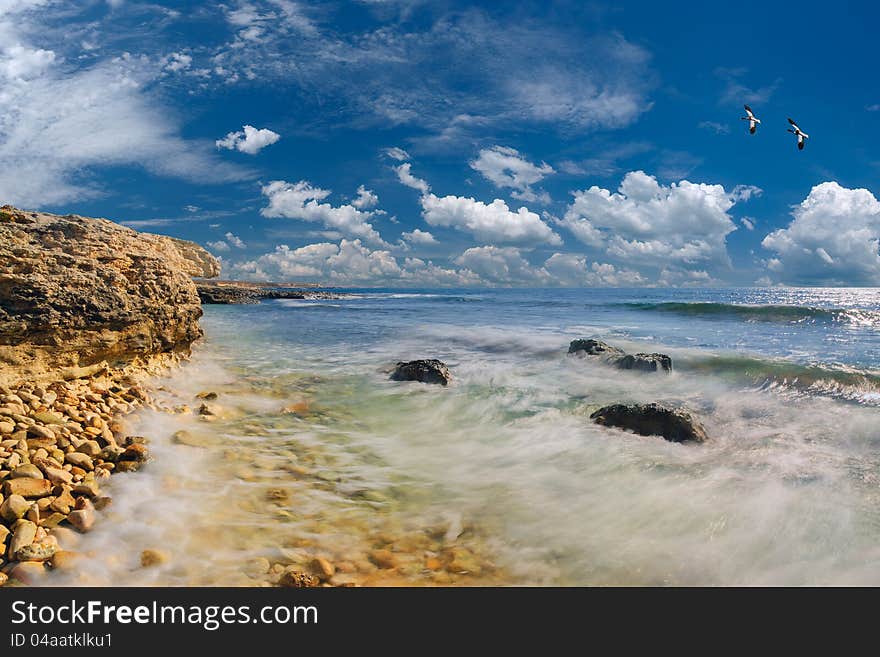 Seascape: sea and rocky coast, in the sky ducks fly, beautiful clouds on background