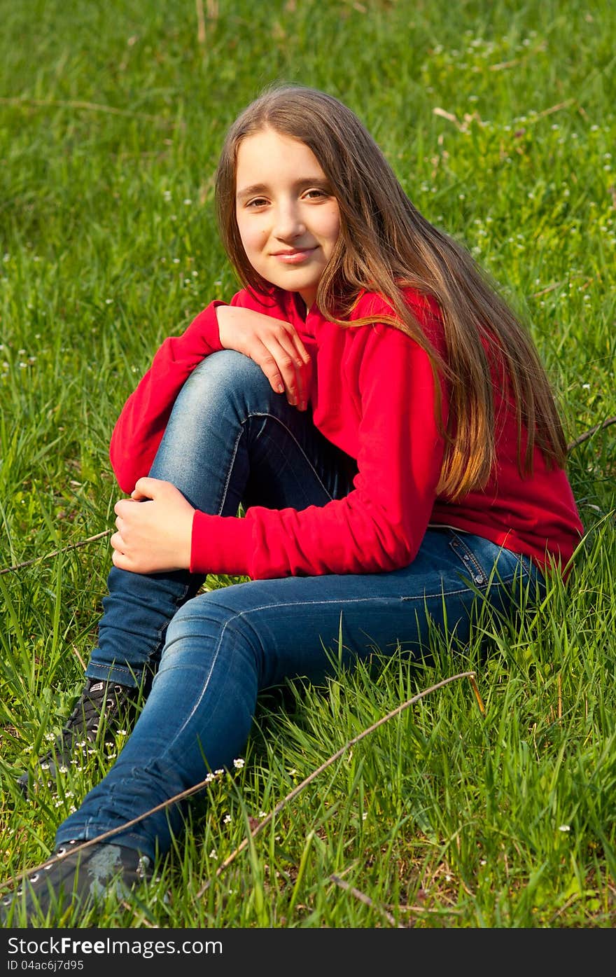 Beautiful teenage girl sitting in the grass on sunny spring day.