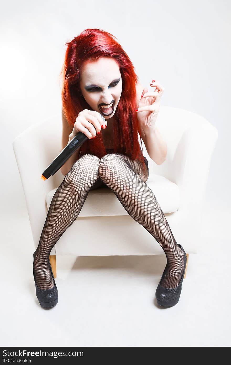 Studio shot of expressive gothic red haired woman with artistic makeup screaming to the microphone over white background. Studio shot of expressive gothic red haired woman with artistic makeup screaming to the microphone over white background