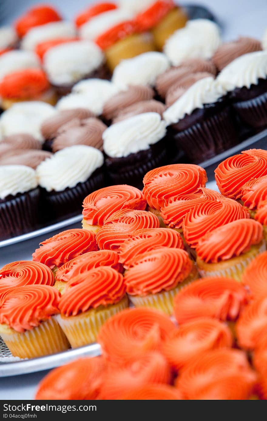 A whole bunch of cupcakes in orange and white. very shallow depth of field