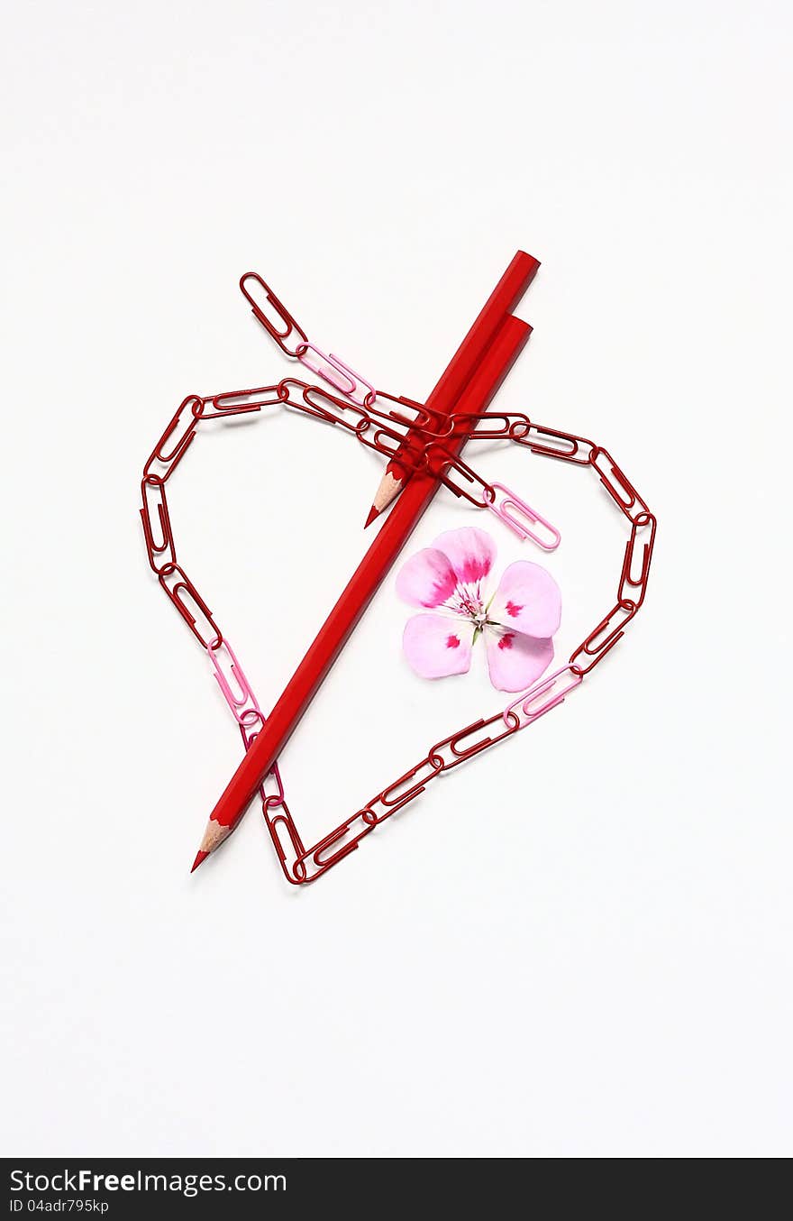 Abstract heart from paper clips is pierced by pencils.Nearby a flower.Background white. Abstract heart from paper clips is pierced by pencils.Nearby a flower.Background white.