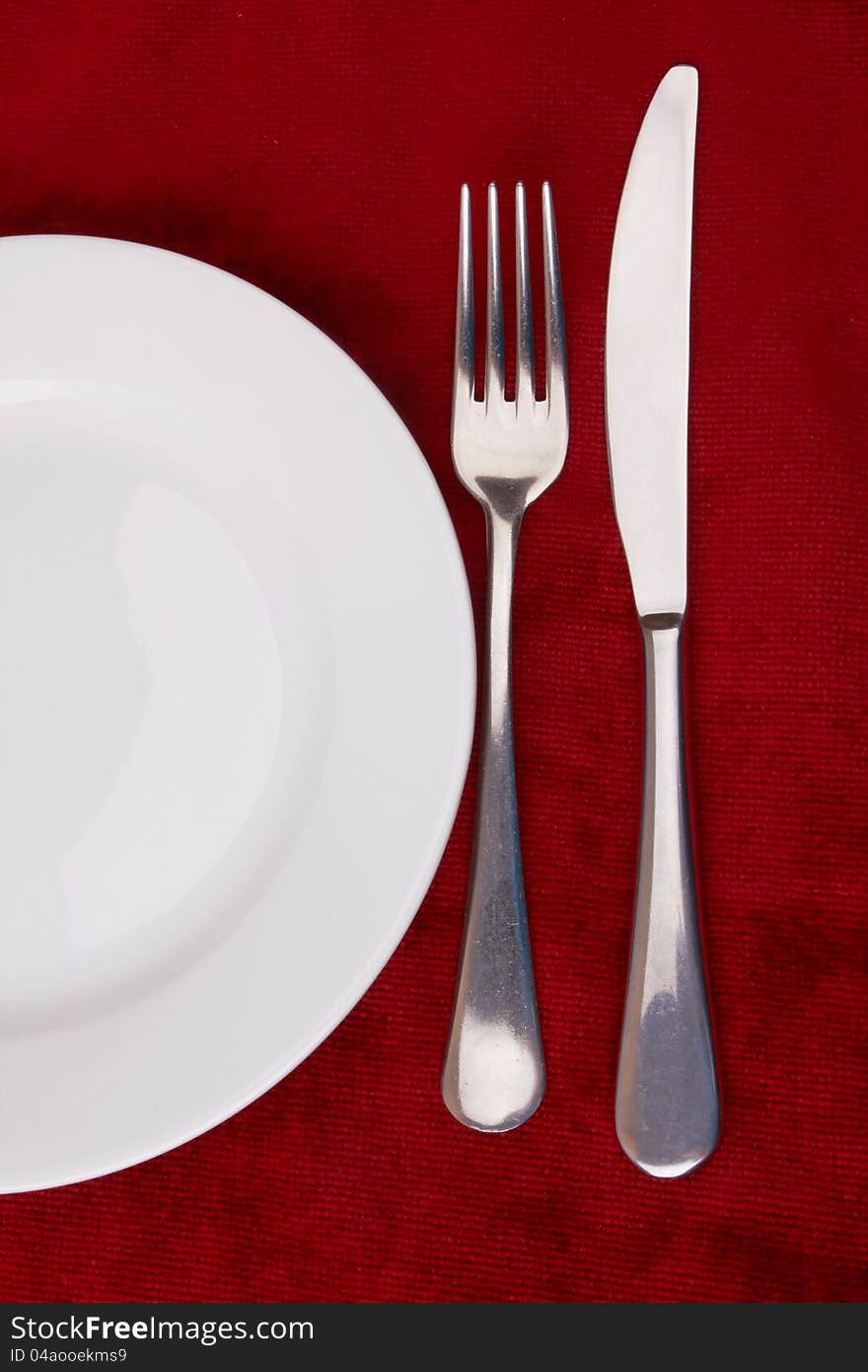 White plate, fork and knife on red background.