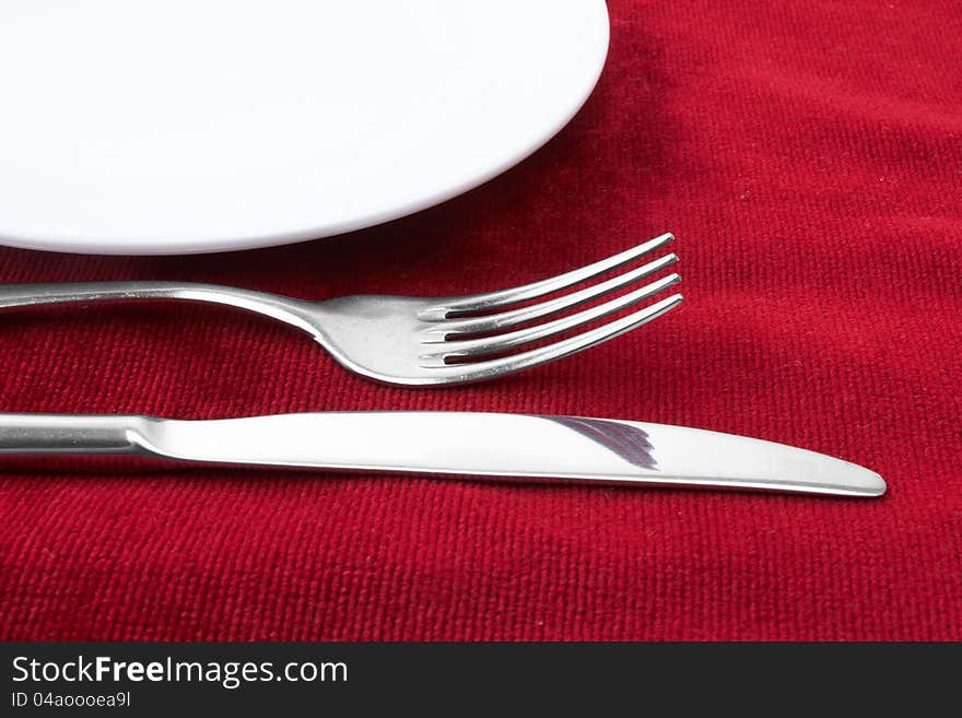 White plate fork and knife on red background.