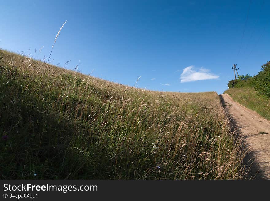 Farm lane leads through the fields to the horizon with a blue sky and a lonely cloud. Farm lane leads through the fields to the horizon with a blue sky and a lonely cloud