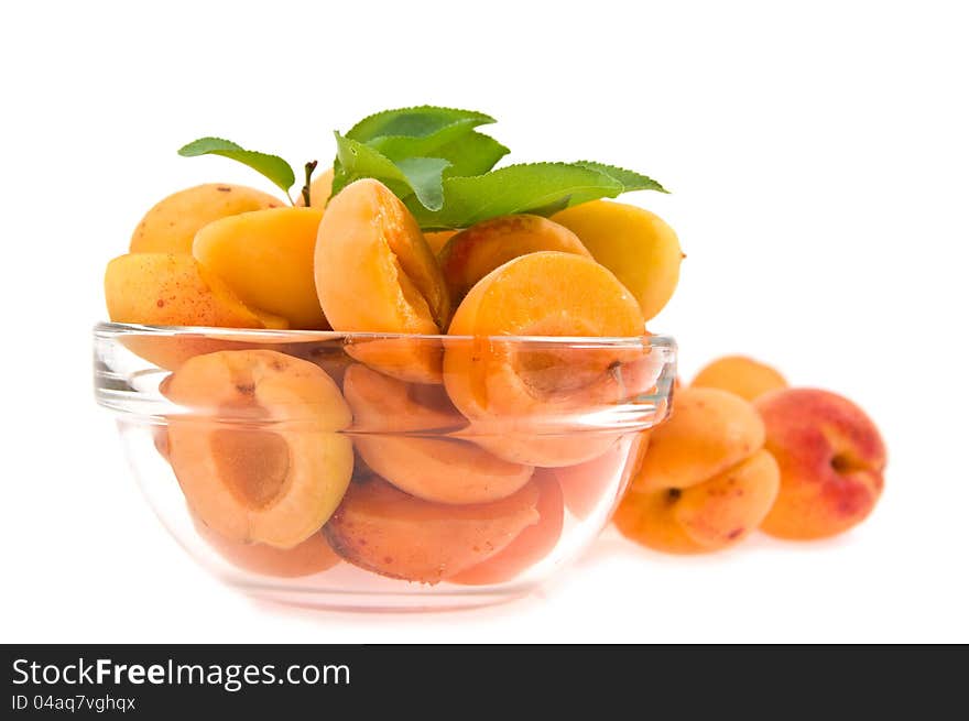 Halves apricot with a green branch in a transparent dish on a white background. Halves apricot with a green branch in a transparent dish on a white background