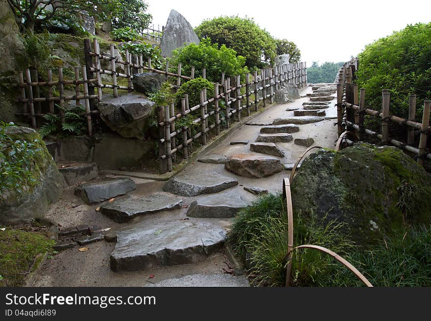Stepping stone path bordered by bamboo fence ascends slope in Japan's ancient Korakuen Garden. horizontal landscape. Stepping stone path bordered by bamboo fence ascends slope in Japan's ancient Korakuen Garden. horizontal landscape.