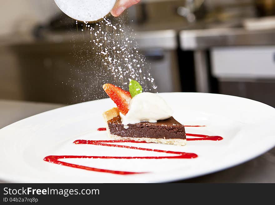 Closeup Dark chocolate tart on a plate decorated with mint leafs and strauberrie a la mode, sprinkled with shugar powder. Closeup Dark chocolate tart on a plate decorated with mint leafs and strauberrie a la mode, sprinkled with shugar powder