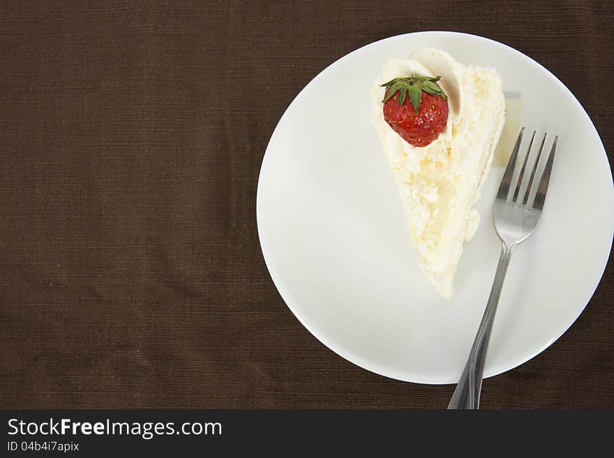 Delicious vanilla cake with strawberry decorate on top, on brown table mat, top view. Delicious vanilla cake with strawberry decorate on top, on brown table mat, top view