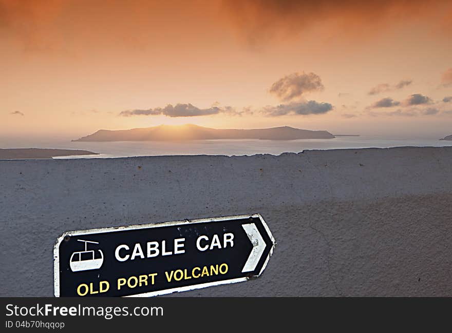 Sign for the cable car at Santorini island in Greece and the volcano during the sunset. Sign for the cable car at Santorini island in Greece and the volcano during the sunset