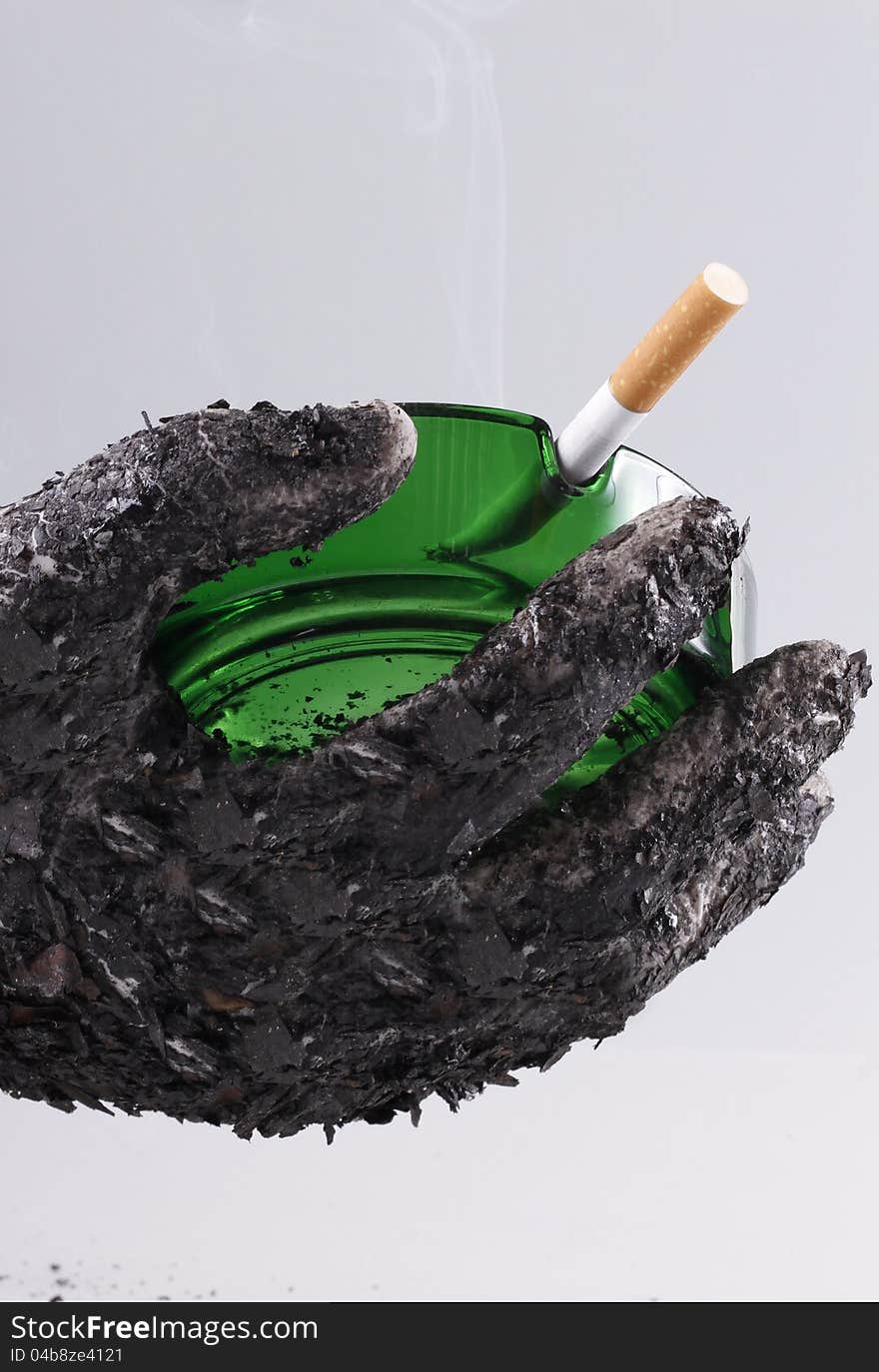 Ashed hand holding green ashtray with a fired cigarette which shows that smoking is harmful. Ashed hand holding green ashtray with a fired cigarette which shows that smoking is harmful