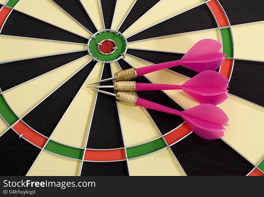 Three pink darts and circular dart board. Three pink darts and circular dart board