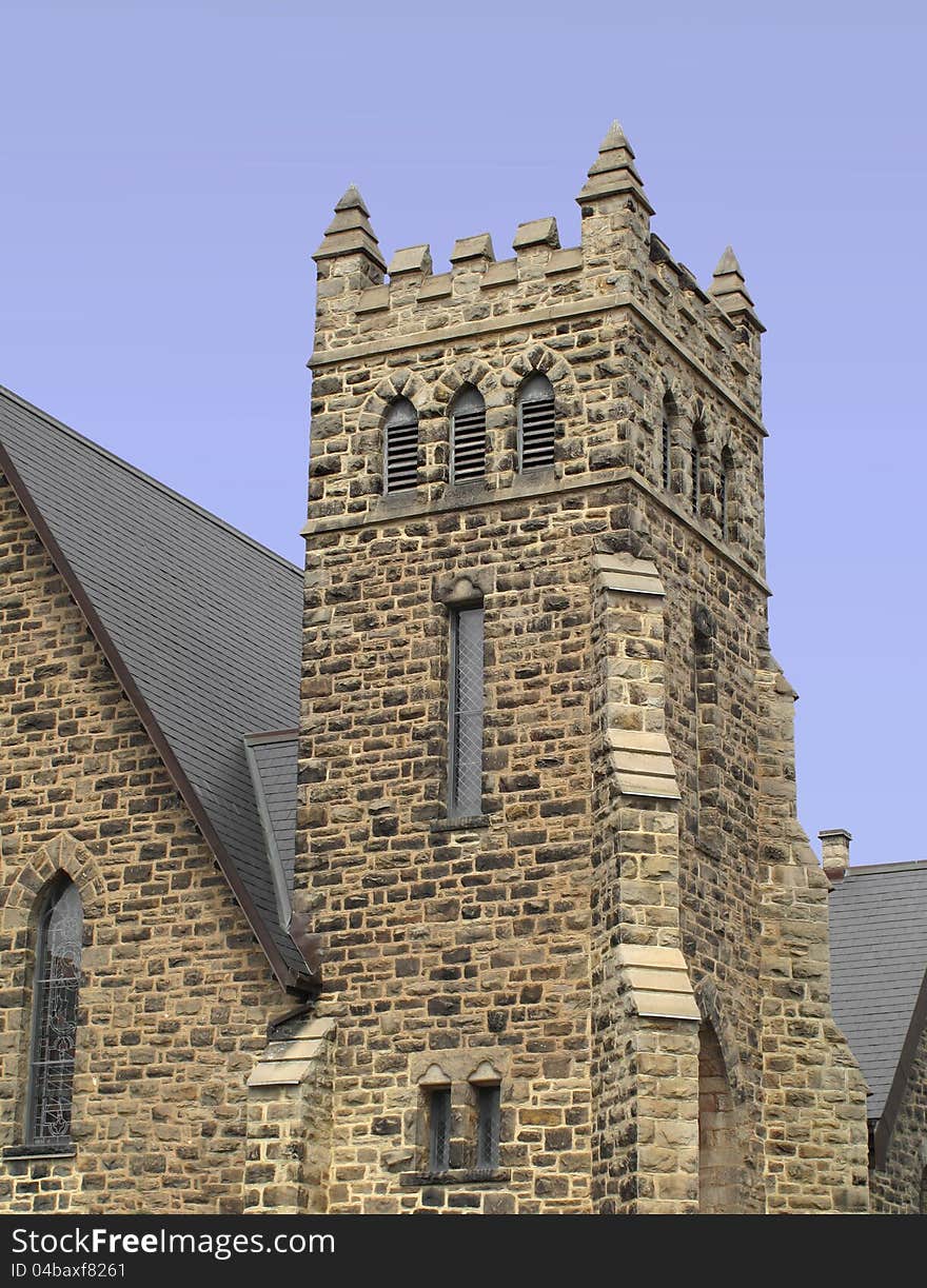 Square stone block fortress type bell tower on the corner of a church. Isolated against a blue sky. Square stone block fortress type bell tower on the corner of a church. Isolated against a blue sky.