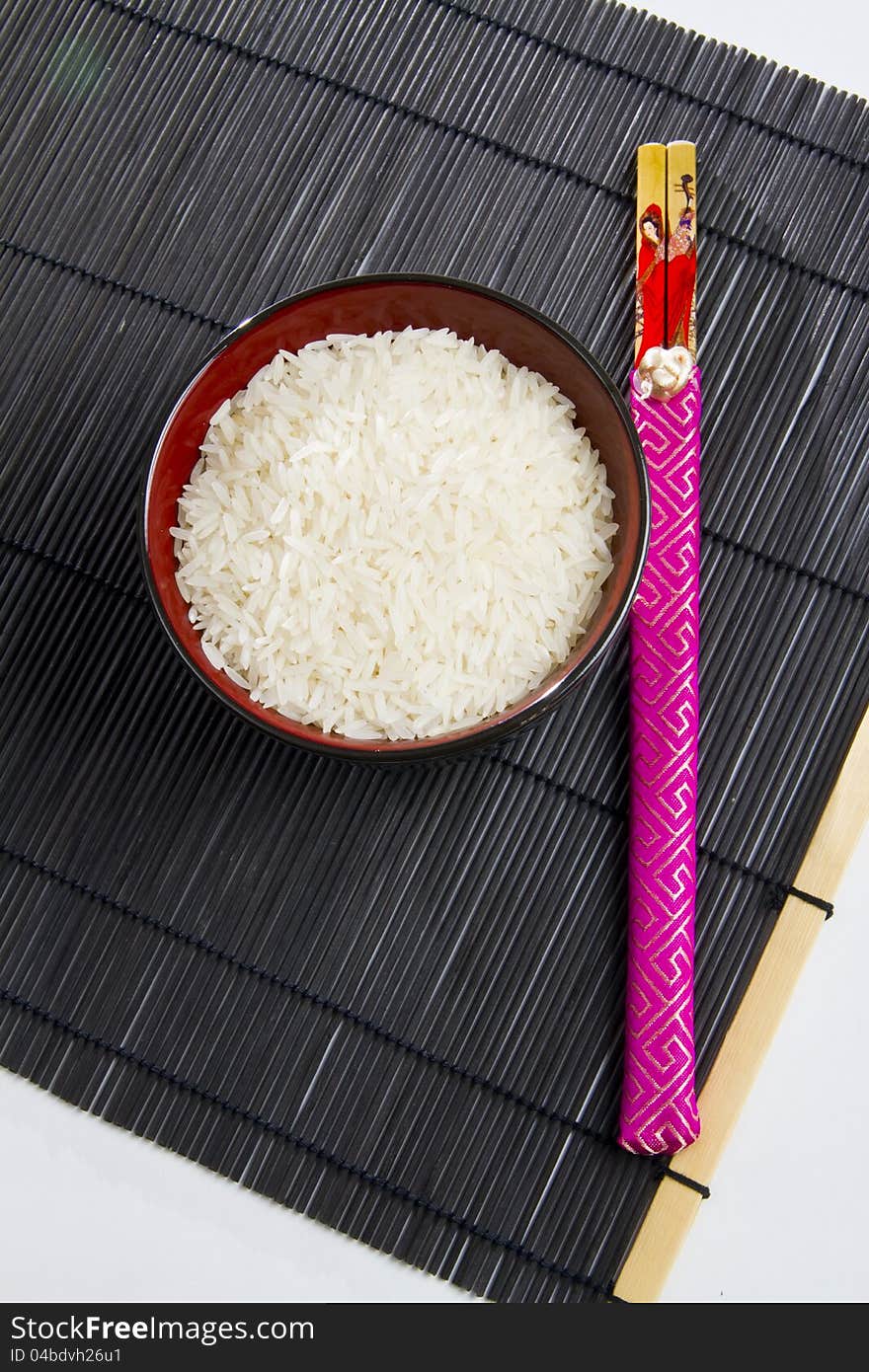 Bowl of rice with chopsticks from top on a black mat