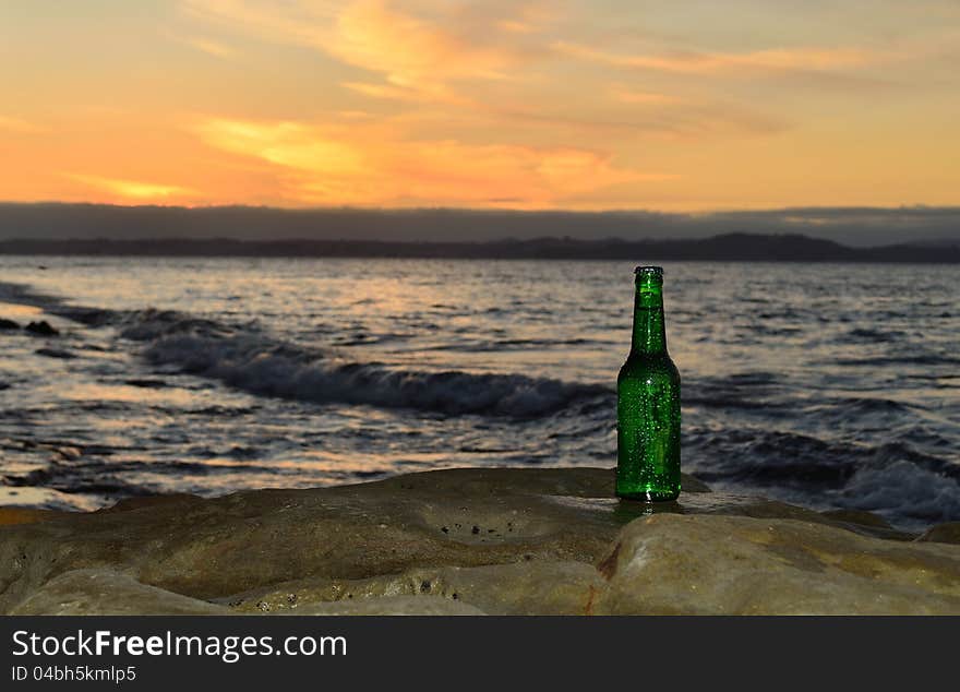 A wet beer bottle on the rocks at sunset. A wet beer bottle on the rocks at sunset.