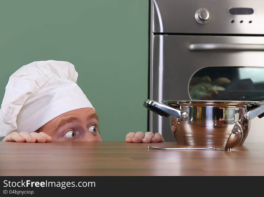 Funny young chef strange looking at pot