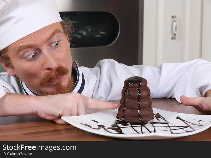 Funny young chef strange looking at piece of cake with chocolate sauce