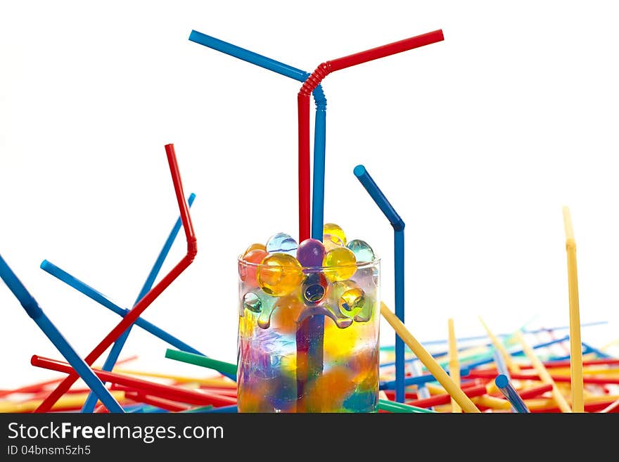 Multicolored straws and a  glass with silicone balls on white ground. Multicolored straws and a  glass with silicone balls on white ground