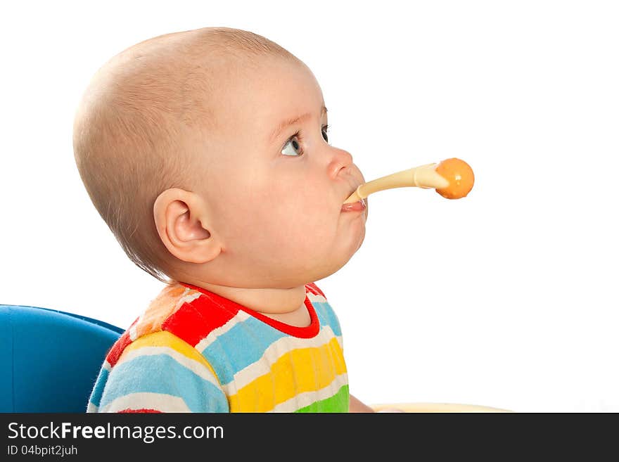 Little baby girl is sitting at the table with spoon in the mouth