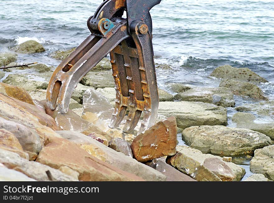 A powerful hydraulic machine has been applied for lifting and moving the rocks. these piles of rock are arranged to form concrete wall so as to prevent coastal erosion. iron pincers. a dredger.