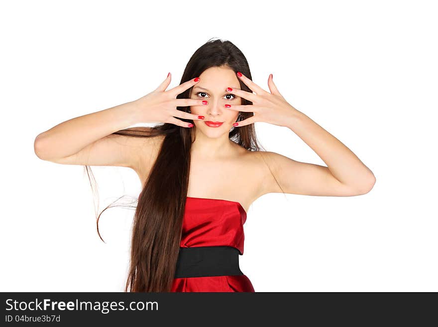 Beautiful girl wearing long red dress looks through her fingers in white studio. Beautiful girl wearing long red dress looks through her fingers in white studio