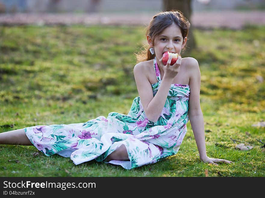 Young Girl Sits On A Meadow And Eats An Apple