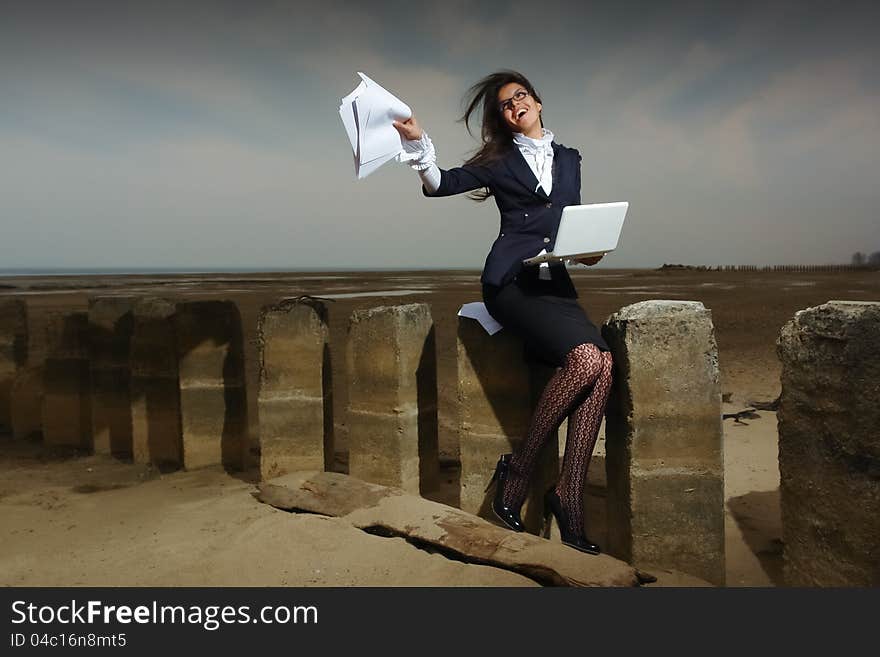 Business lady sitting on the beach, on a background cloudy sky. She sits on the pile, the wind fluttering her hair. In the hands of her laptop.