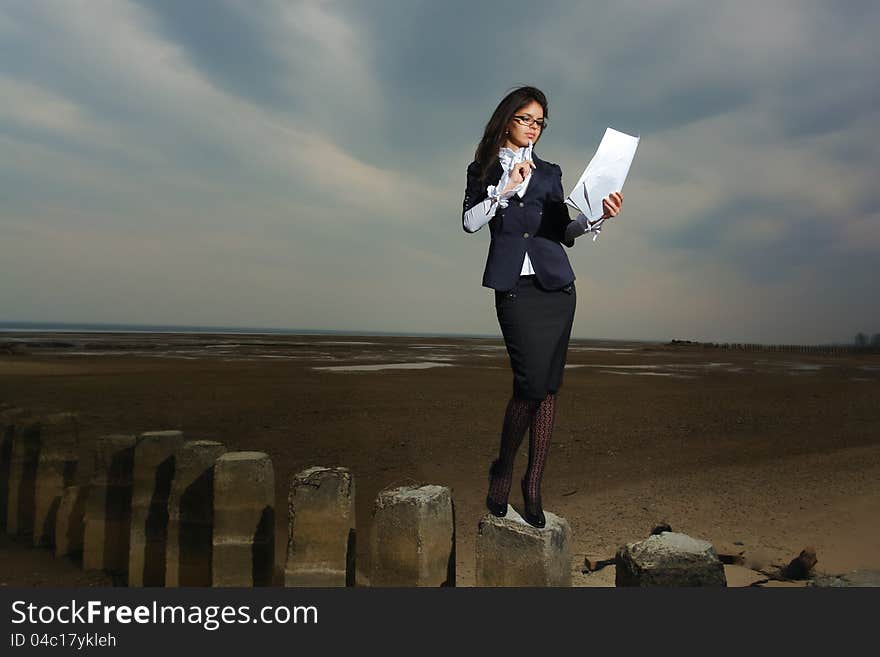 Business lady standing on the beach, on a background cloudy sky. It stands on stilts, the wind fluttering her hair. In the hands of her paper.