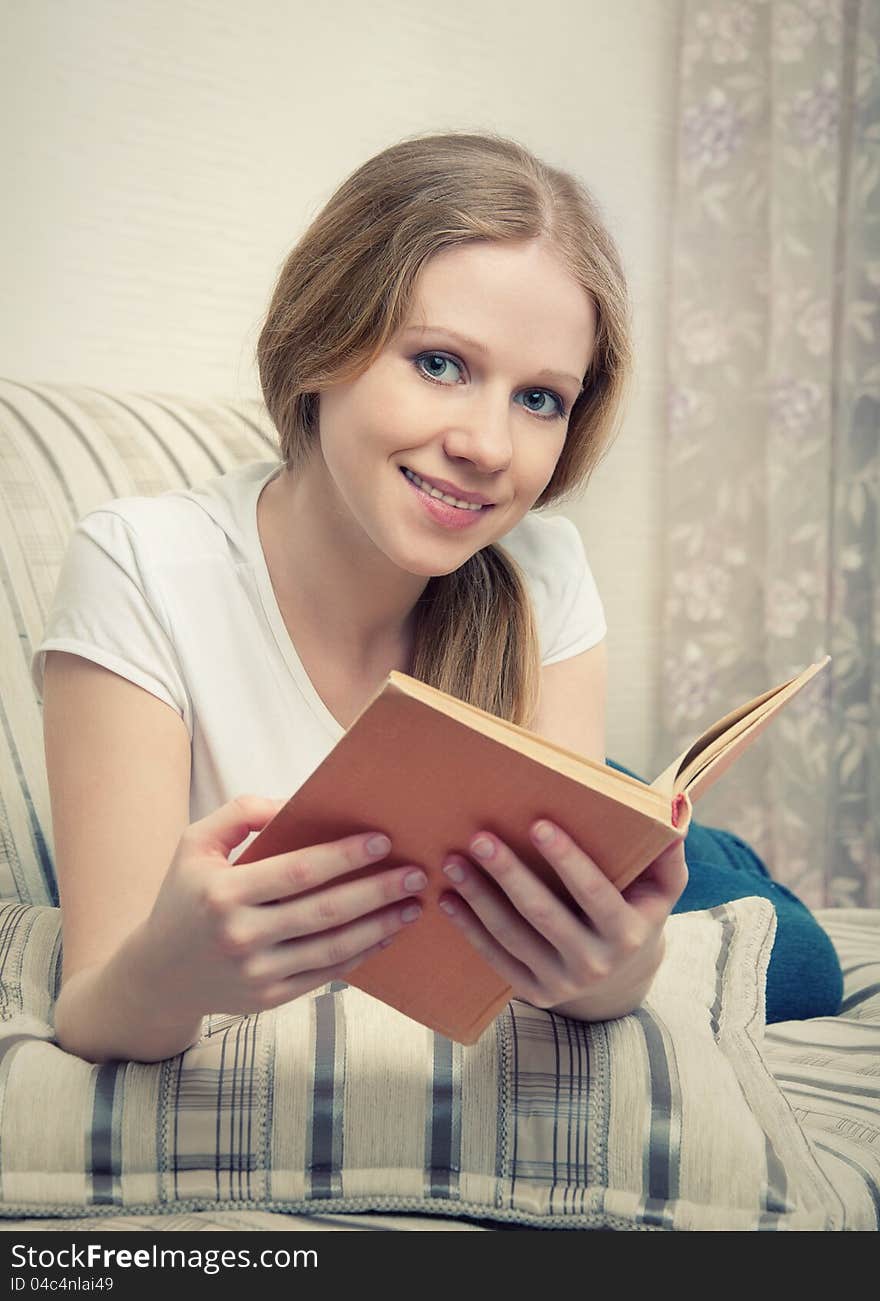 Pretty girl relaxing at home, she reading a book lying on the sofa. Pretty girl relaxing at home, she reading a book lying on the sofa