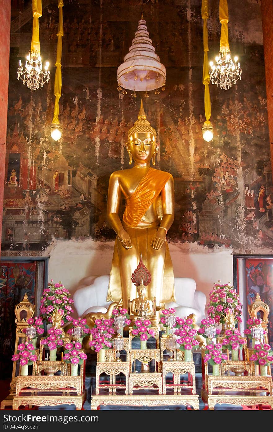 Sitting gold buddha statue with antique hanging lamp and mural painting in the background