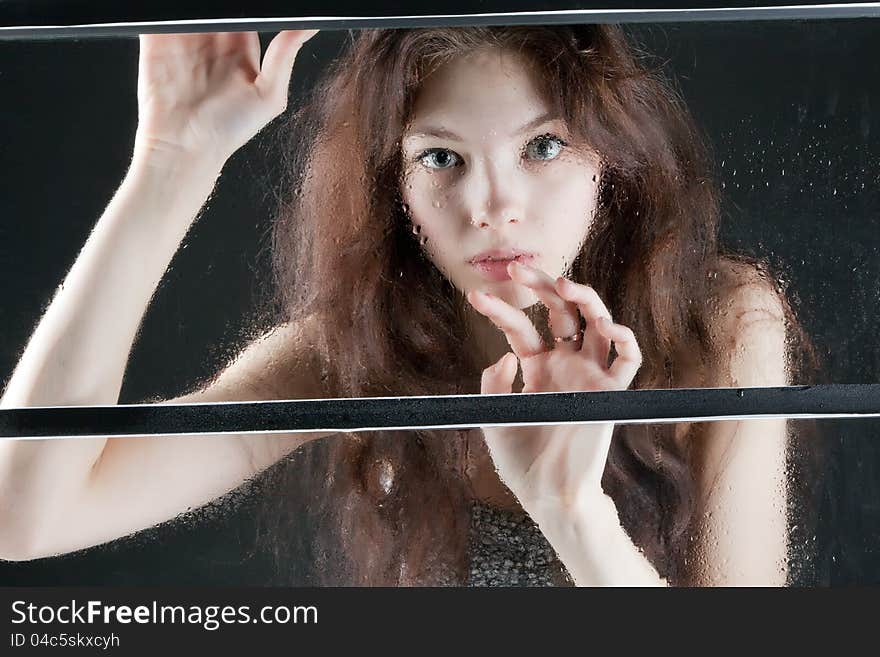 Portrait of a beautiful girl in a wet window on a dark background. Portrait of a beautiful girl in a wet window on a dark background