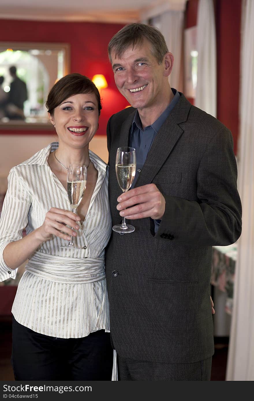 Happy smiling romantic couple standing side by side with champagne glasses in their hands in romantic red interior.