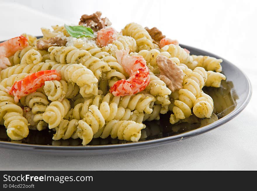 A black dish with pasta with pesto and parmesan cheese on white table