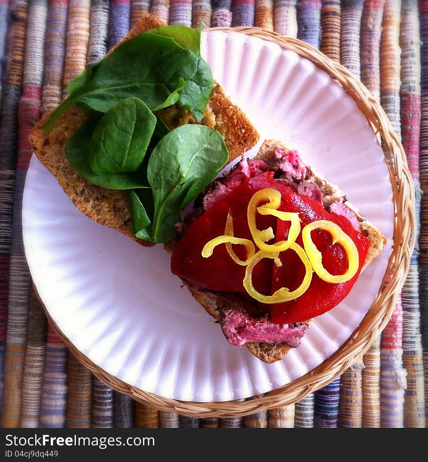 A sliced grilled steak sandwich with baby spinach, roasted red peppers and hot pepper rings on whole grain Ciabatta bread. The sandwich is sitting on a white paper plate. A sliced grilled steak sandwich with baby spinach, roasted red peppers and hot pepper rings on whole grain Ciabatta bread. The sandwich is sitting on a white paper plate.