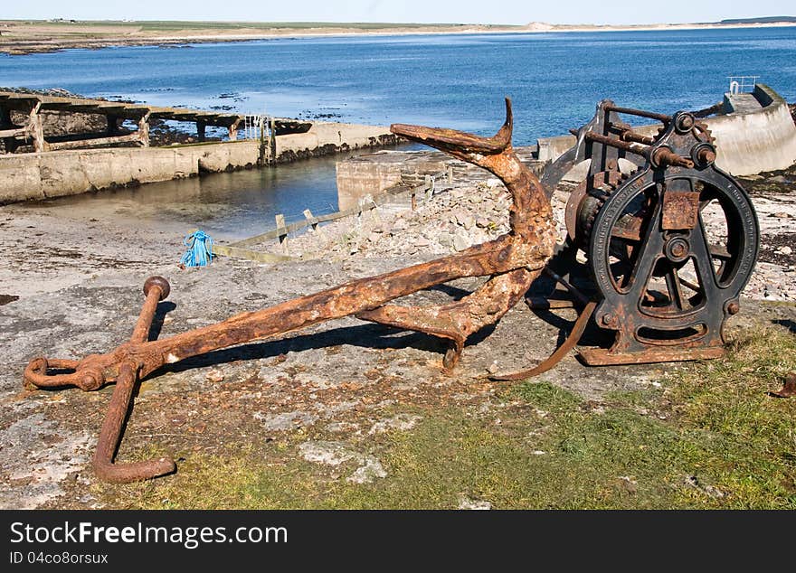 Anchor and a winch,Sinclair Bay, Auckergill, Caithness, Scotland,UK. An anchor windlass is a machine that restrains and manipulates the anchor chain on a boat, allowing the anchor to be raised and lowered by means of chain cable. A notched wheel engages the links of the chain or the rope. Crown-The pointed end of the anchor which attaches the shank to the arms. Eye-Hole at the end of the shank through which the ring is attached. Fluke-The spade-shaped appendage of the arm used for digging into the sea bed to secure the vessel. The palm-Flat uppermost portion of the fluke. A deadman anchor is a buried object like a log, rock, or pack. The strength of the deadman anchor depends on The perpendicular cross-sectional area of the object that is buried. Anchor and a winch,Sinclair Bay, Auckergill, Caithness, Scotland,UK. An anchor windlass is a machine that restrains and manipulates the anchor chain on a boat, allowing the anchor to be raised and lowered by means of chain cable. A notched wheel engages the links of the chain or the rope. Crown-The pointed end of the anchor which attaches the shank to the arms. Eye-Hole at the end of the shank through which the ring is attached. Fluke-The spade-shaped appendage of the arm used for digging into the sea bed to secure the vessel. The palm-Flat uppermost portion of the fluke. A deadman anchor is a buried object like a log, rock, or pack. The strength of the deadman anchor depends on The perpendicular cross-sectional area of the object that is buried.