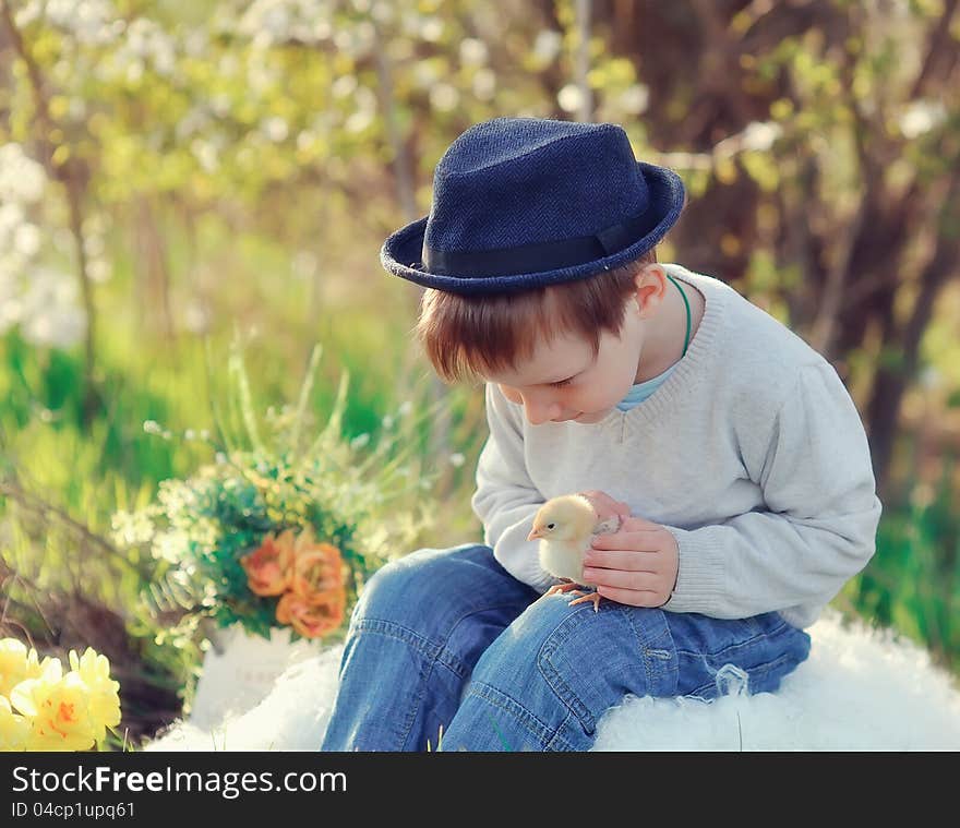 The boy outdoors in a hat plays with chickens. The boy outdoors in a hat plays with chickens