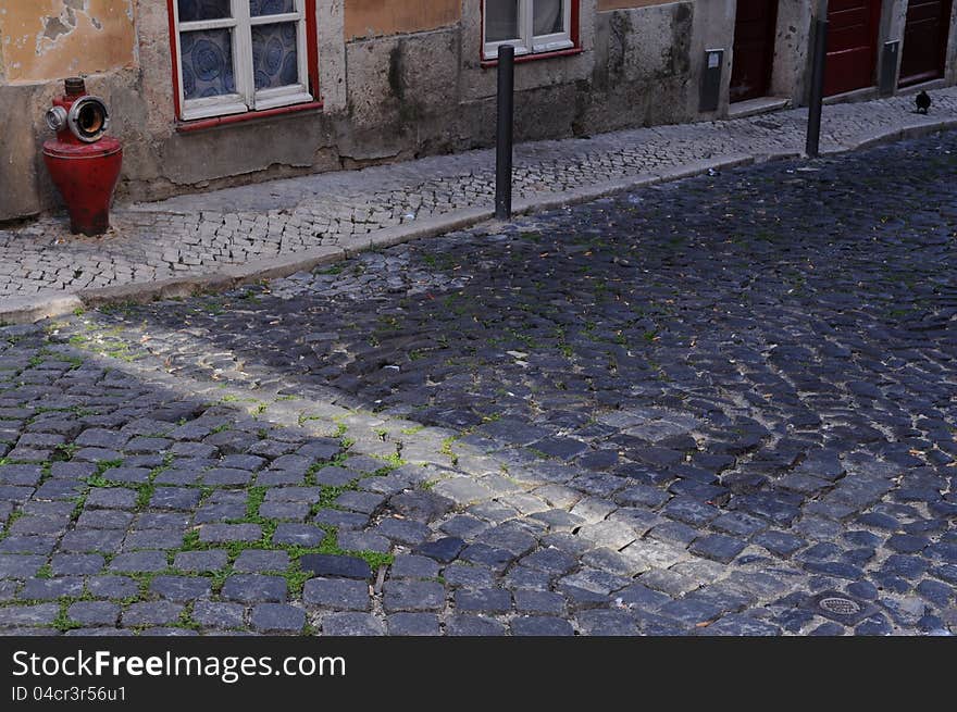 Cobblestone street with a ray of sunshine, with an old red fire hydrant, in Lisbon. Cobblestone street with a ray of sunshine, with an old red fire hydrant, in Lisbon.