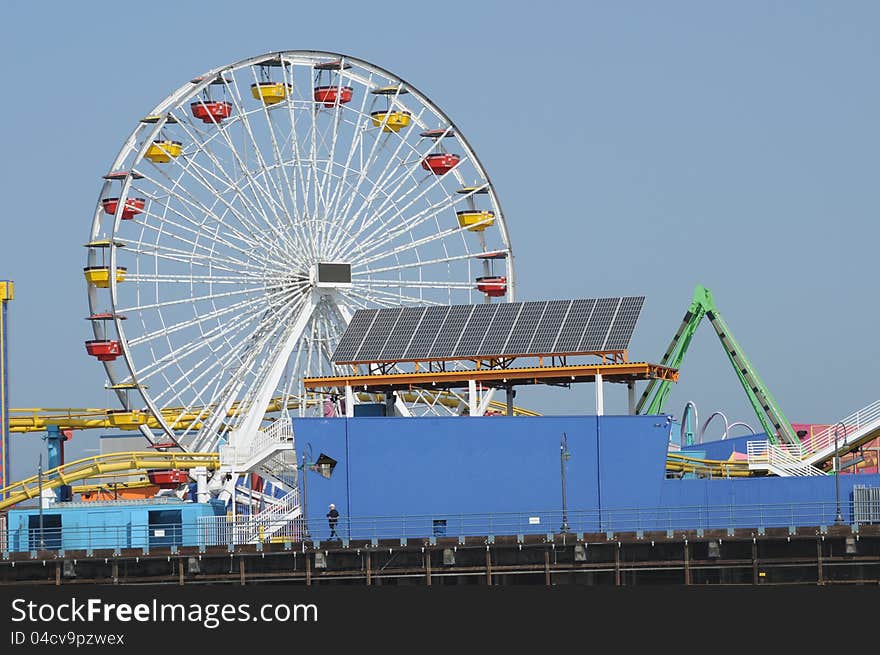 A colorful ferris wheel with red and yellow passenger buckets and solar panels  next to it. A colorful ferris wheel with red and yellow passenger buckets and solar panels  next to it