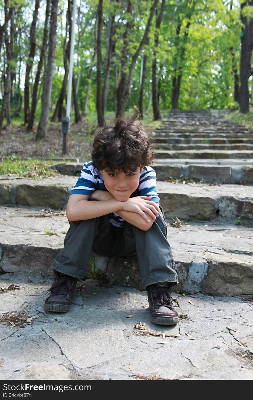 Beautiful smiling boy sitting resting on stone staircase with arms propped on his head. Beautiful smiling boy sitting resting on stone staircase with arms propped on his head