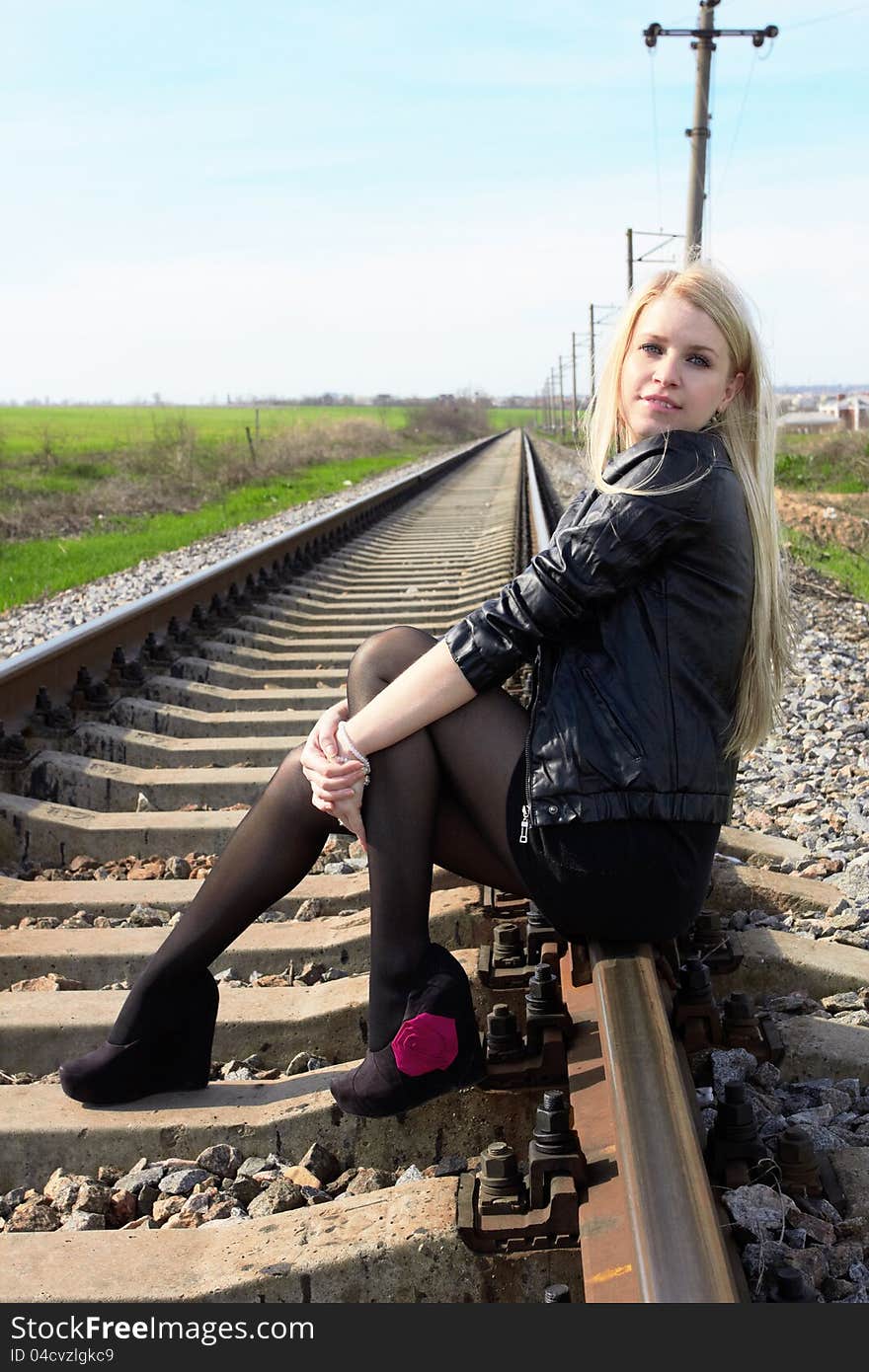 Attractive young girl sitting on railroad tracks