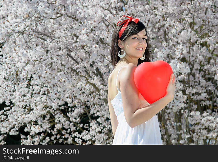 Young beautiful woman with red heart shape balloon and trees in bloom. Young beautiful woman with red heart shape balloon and trees in bloom