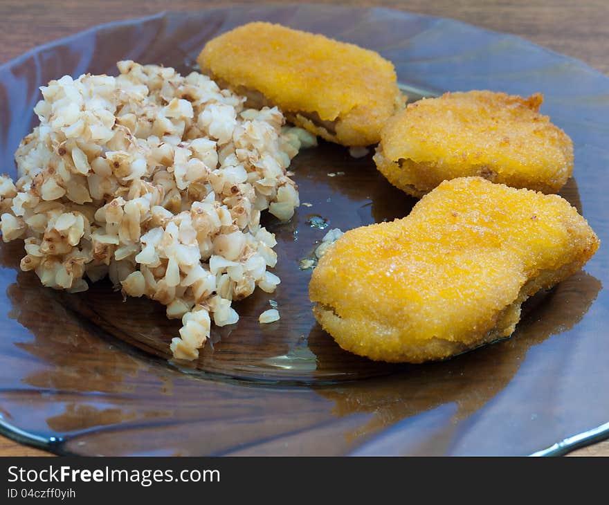 A plate of buckwheat porridge with chicken nuggets standing on a wooden table for the dinner.