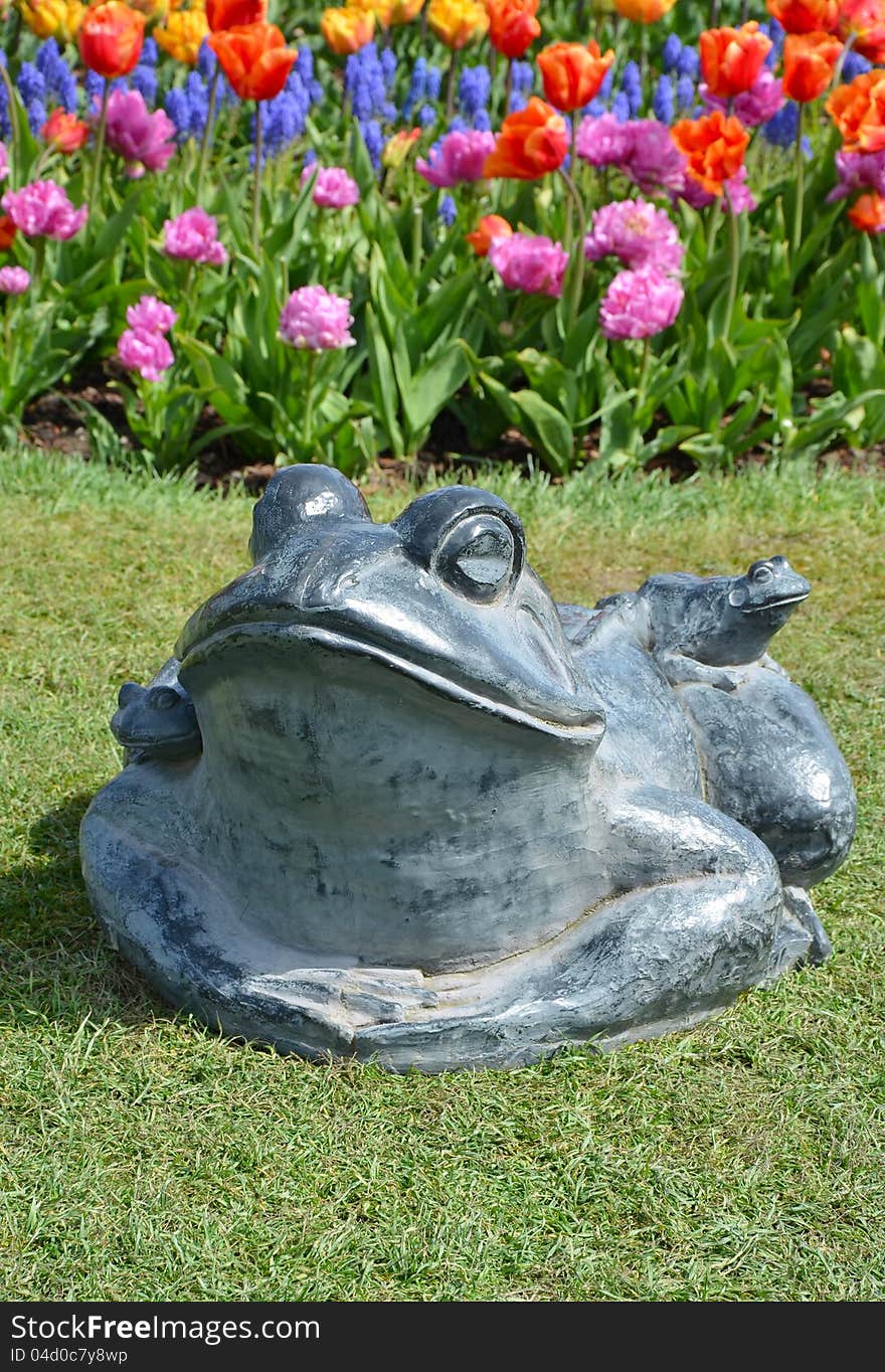 Stone frog in colorful spring garden