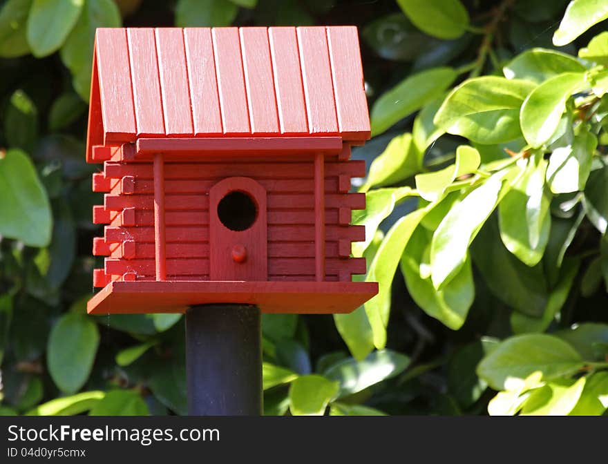 Barn Red Birdhouse Mounted On Pole With Green Leaf Background. Barn Red Birdhouse Mounted On Pole With Green Leaf Background